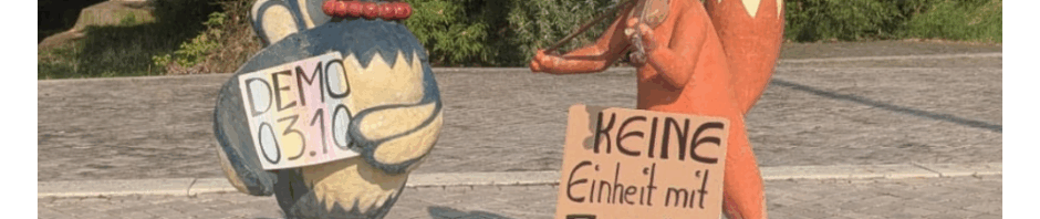 Die Kika-Figuren Herr Fuchs und Frau Elster werben für die Demo gegen die AfD am 3. Oktober. Sie halten Schilder mit "Demo 3.10." und "Keine Einheit mit Faschist*innen"